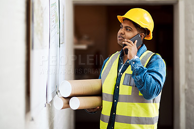 Buy stock photo Shot of a young engineer talking on his cellphone while reading something on a wall