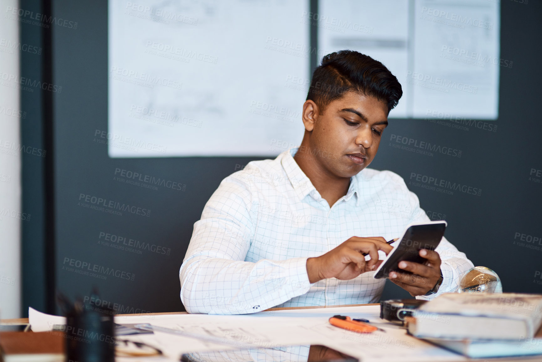 Buy stock photo Shot of a young architect using a calculator while drawing up a building plan