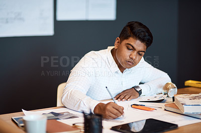 Buy stock photo Shot of a young architect drawing up a building plan in a modern office