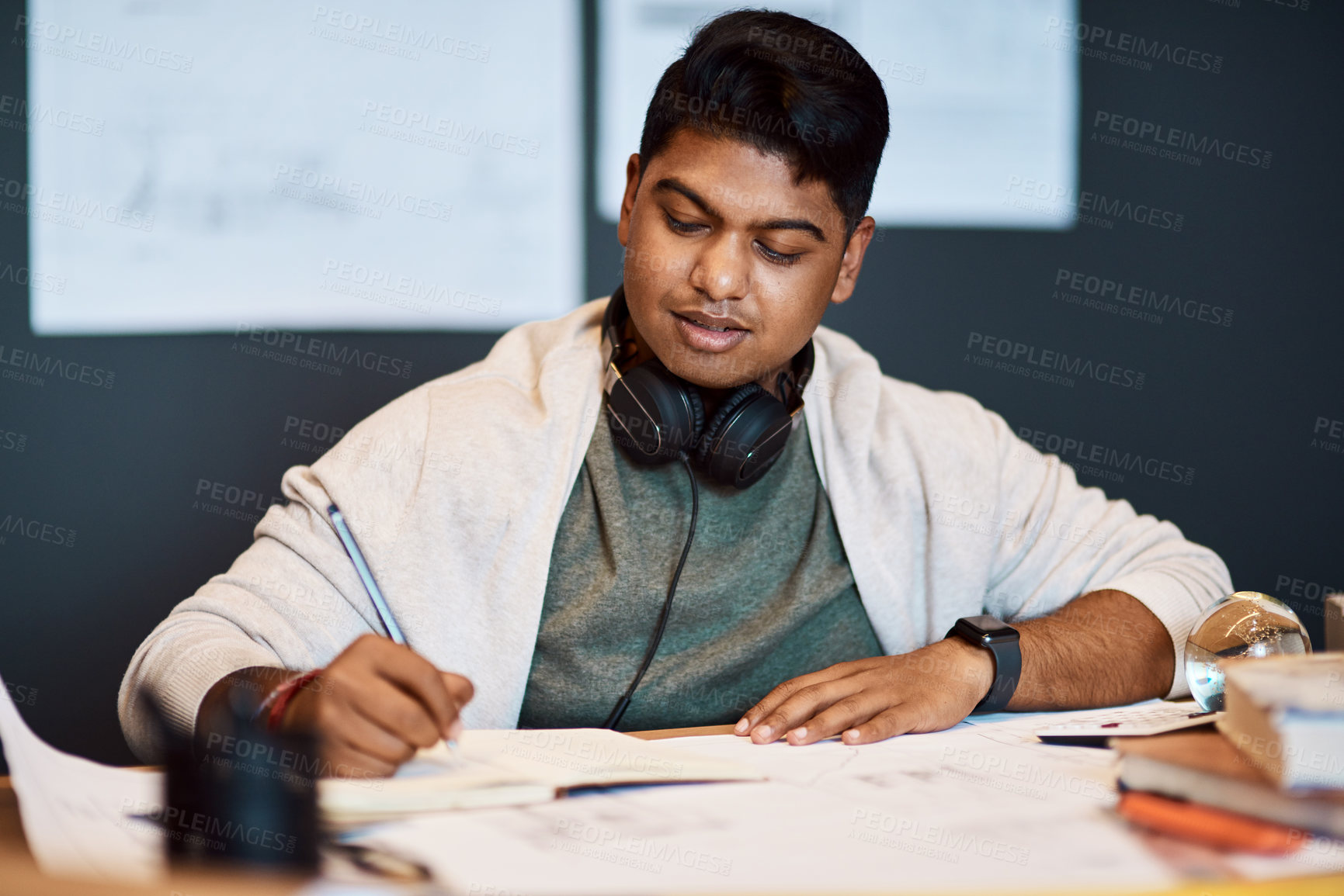 Buy stock photo Shot of a young architect writing in a notebook at his desk in a modern office