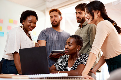 Buy stock photo Shot of a group of young creatives working together on a laptop in an office