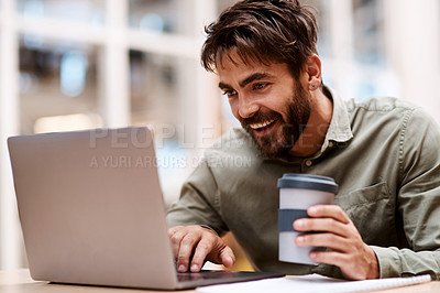 Buy stock photo Shot of a young businessman working a laptop while drinking coffee in an office