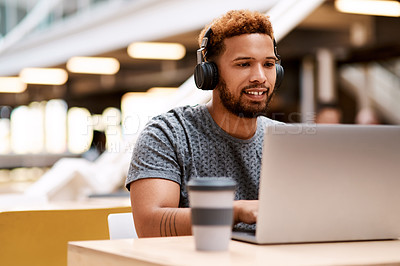 Buy stock photo Shot of a young businessman wearing headphones while working on a laptop in an office