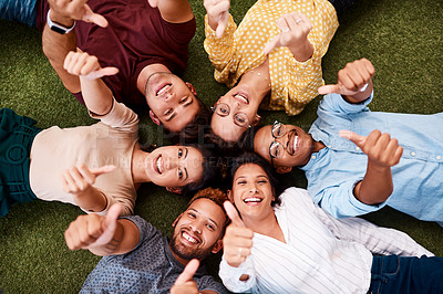 Buy stock photo Portrait of a group of young creatives showing thumbs up while lying down in a huddle together