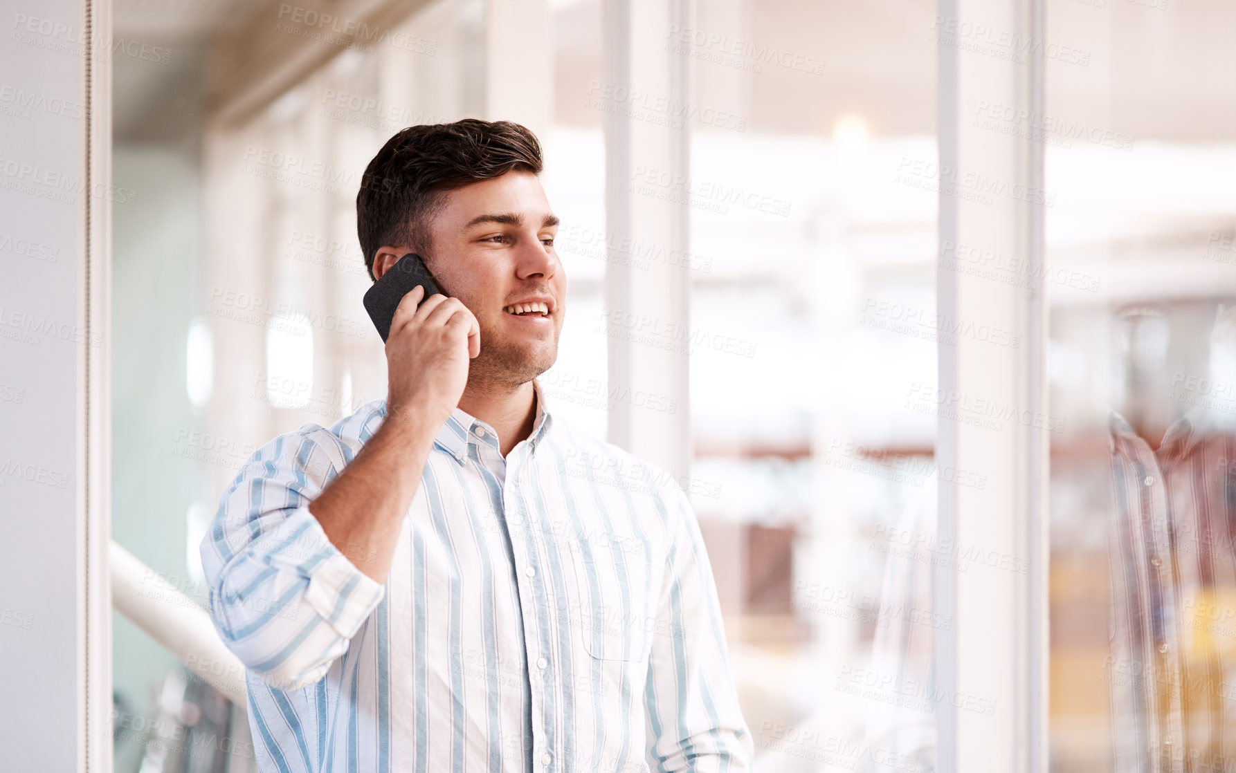 Buy stock photo Cropped shot of a handsome young male designer making a phonecall while standing at at a window in his office