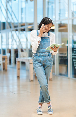 Buy stock photo Shot of a young businesswoman talking on a cellphone while going through a notebook in an office
