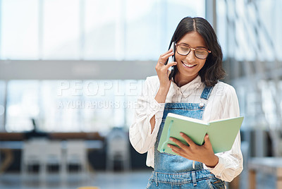 Buy stock photo Shot of a young businesswoman talking on a cellphone while going through a notebook in an office