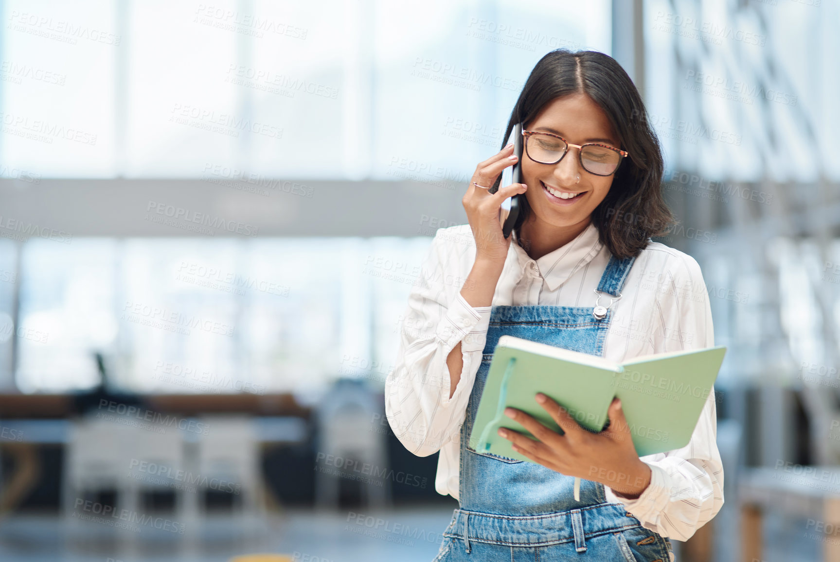 Buy stock photo Shot of a young businesswoman talking on a cellphone while going through a notebook in an office