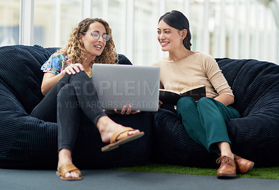 Buy stock photo Shot of two businesswomen using a laptop together while sitting on beanbags in an office