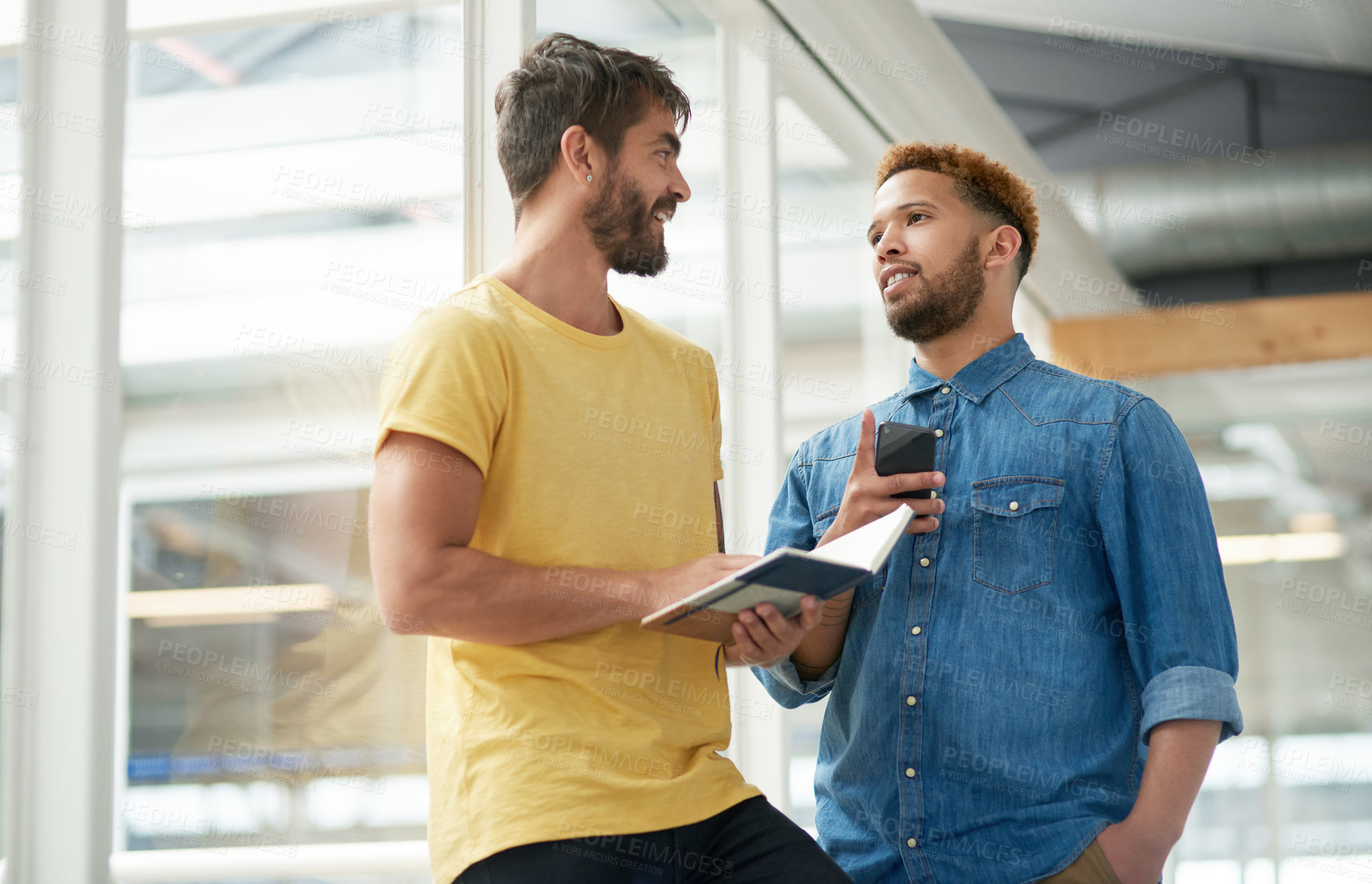 Buy stock photo Shot of two businessmen going through a notebook together in an office