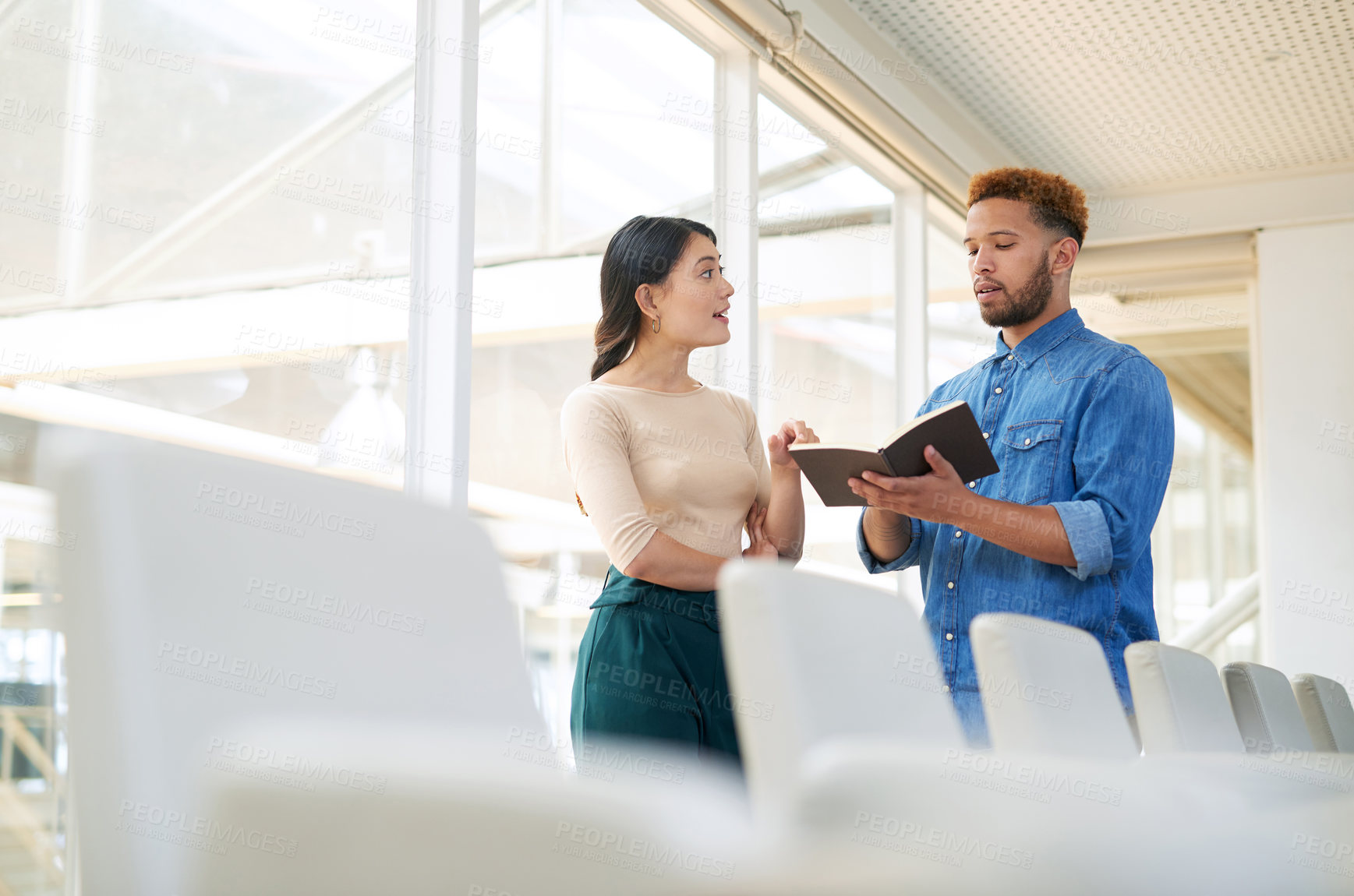 Buy stock photo Shot of two businesspeople going through a notebook together in an office