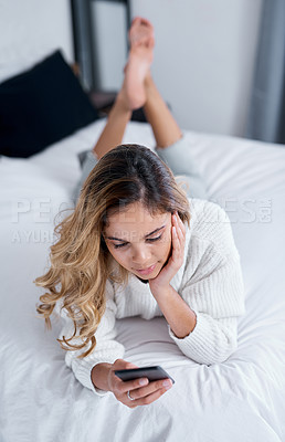 Buy stock photo Shot of a young woman using her cellphone while lying on her bed