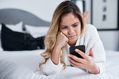 Buy stock photo Shot of a young woman using her cellphone while lying on her bed