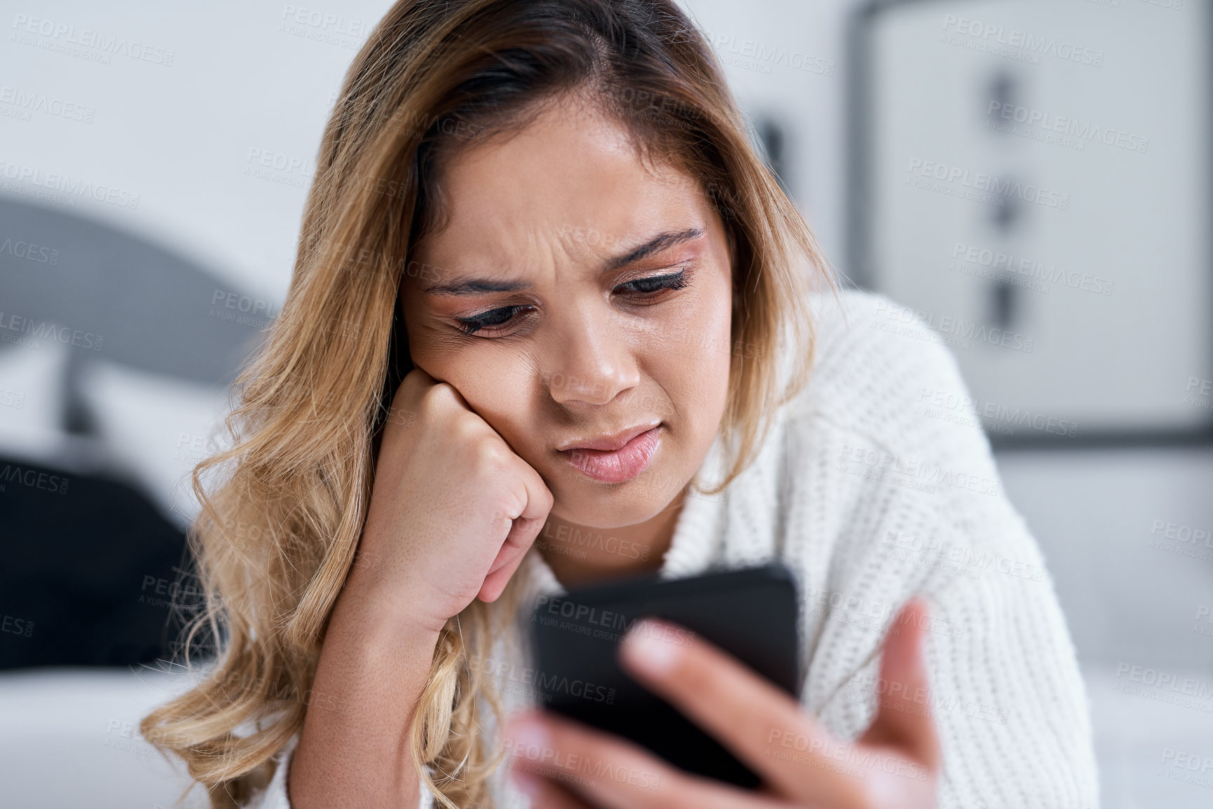 Buy stock photo Shot of a young woman using her cellphone while lying on her bed