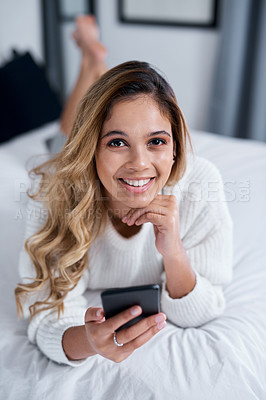 Buy stock photo Shot of a young woman using her cellphone while lying on her bed