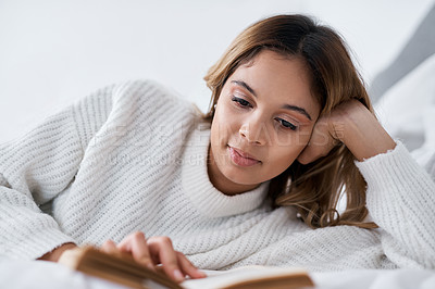 Buy stock photo Cropped shot of a young woman reading a book while lying on her bed