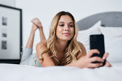 Buy stock photo Shot of a young woman using her cellphone while lying on her bed