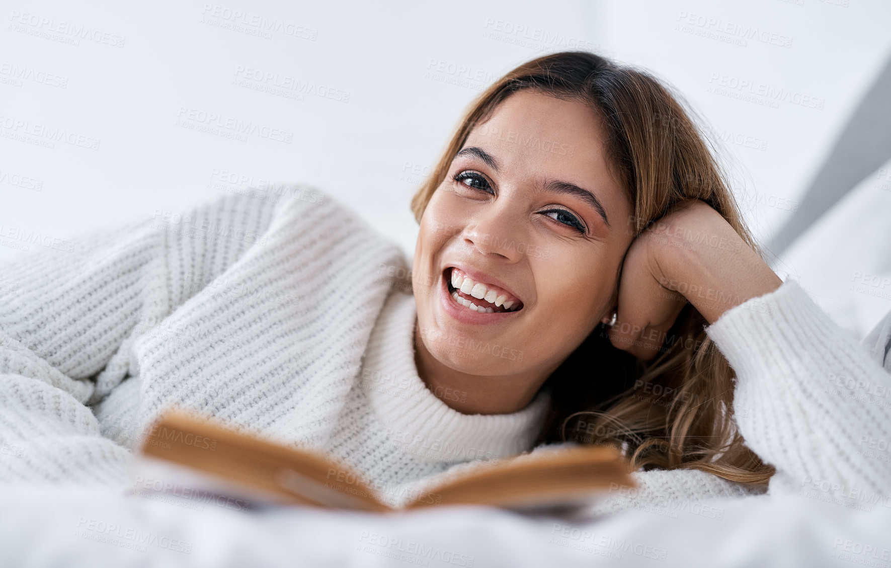 Buy stock photo Portrait of a young woman lying on her bed with a book