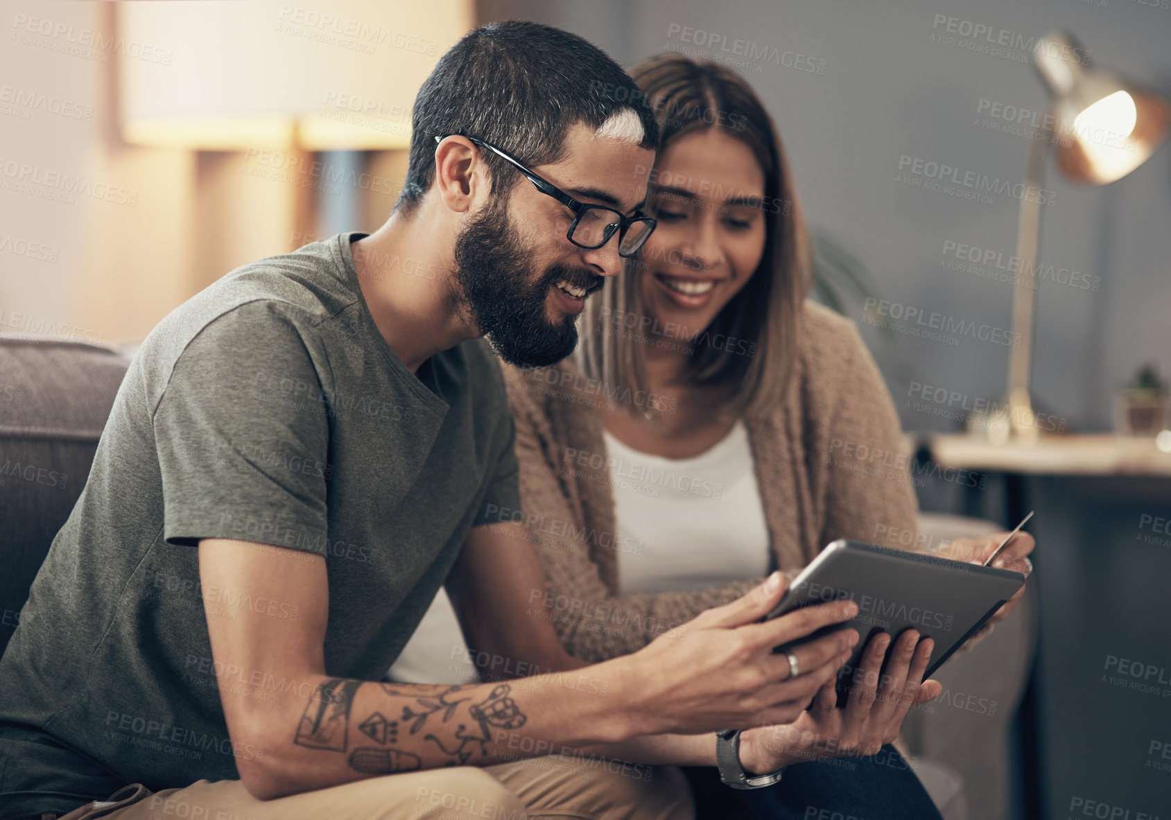 Buy stock photo Shot of a young couple using a digital tablet and credit card on the sofa at home