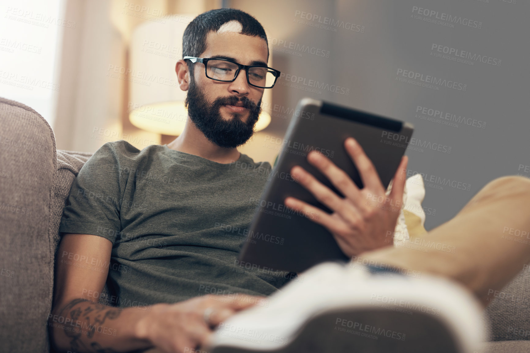 Buy stock photo Shot of a young man using a digital tablet on the sofa at home