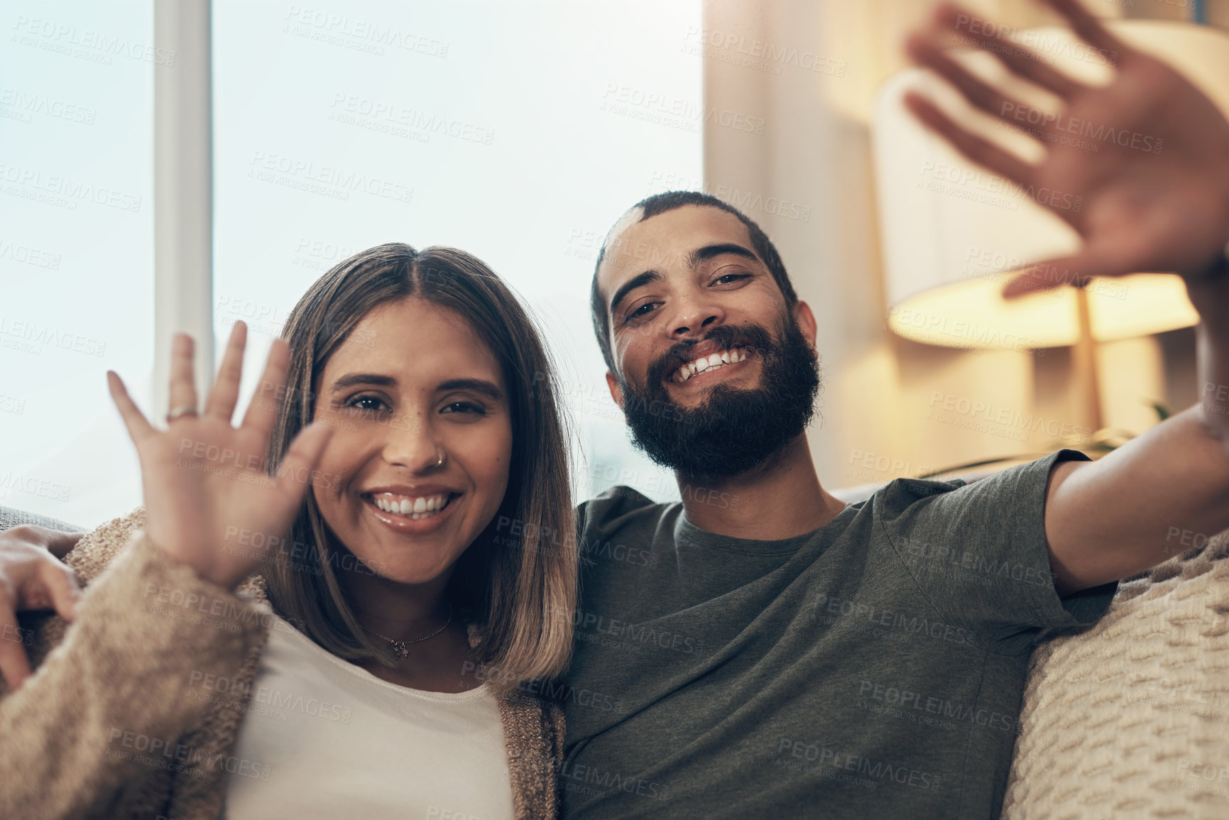 Buy stock photo Portrait of a happy young couple waving during a video call on the sofa at home