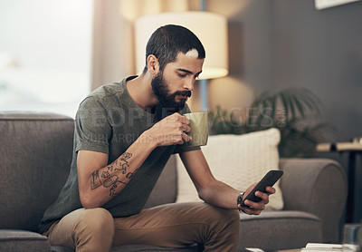 Buy stock photo Shot of a young man having coffee and using a smartphone on the sofa at home