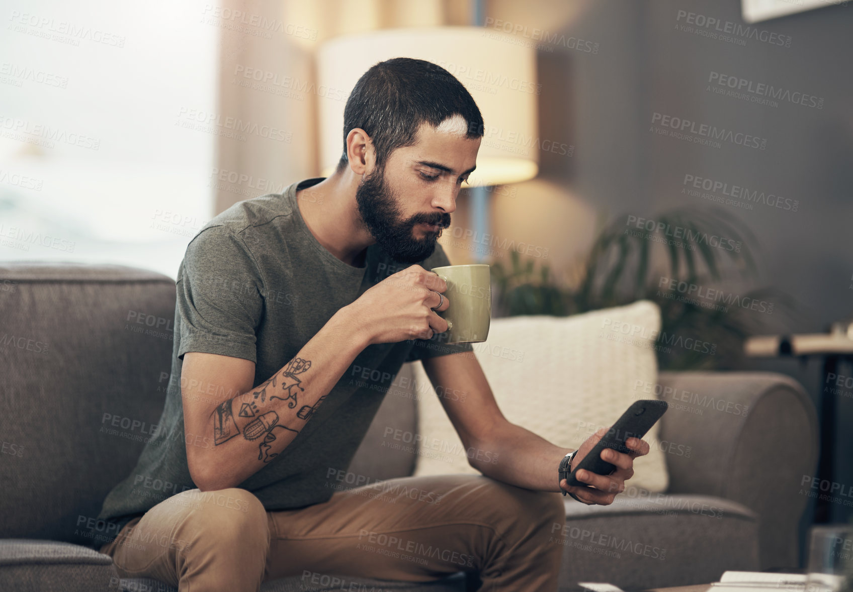 Buy stock photo Shot of a young man having coffee and using a smartphone on the sofa at home