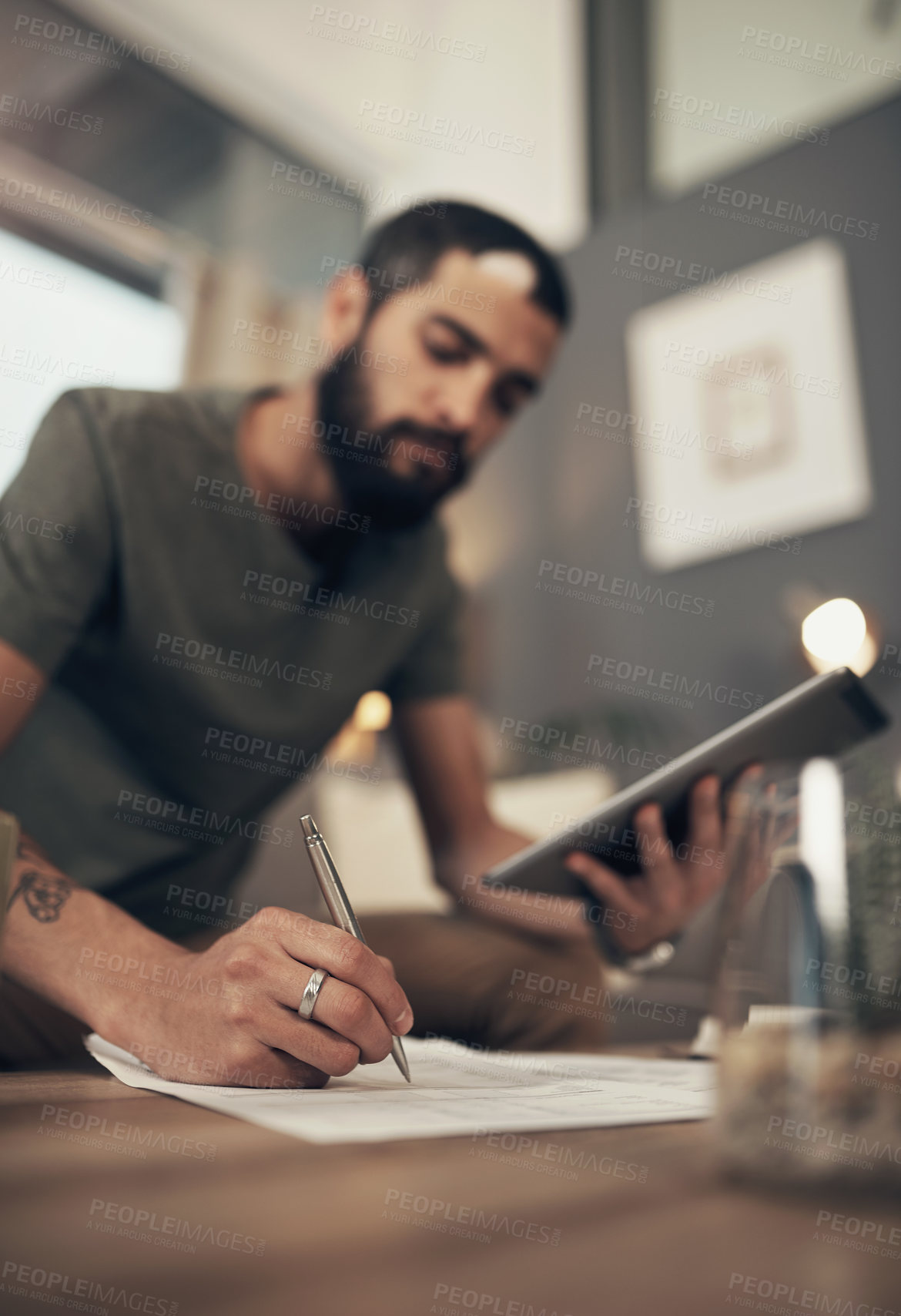 Buy stock photo Shot of a young man using a digital tablet while going through paperwork at home
