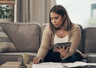 Buy stock photo Shot of a young woman using a digital tablet while going through paperwork at home