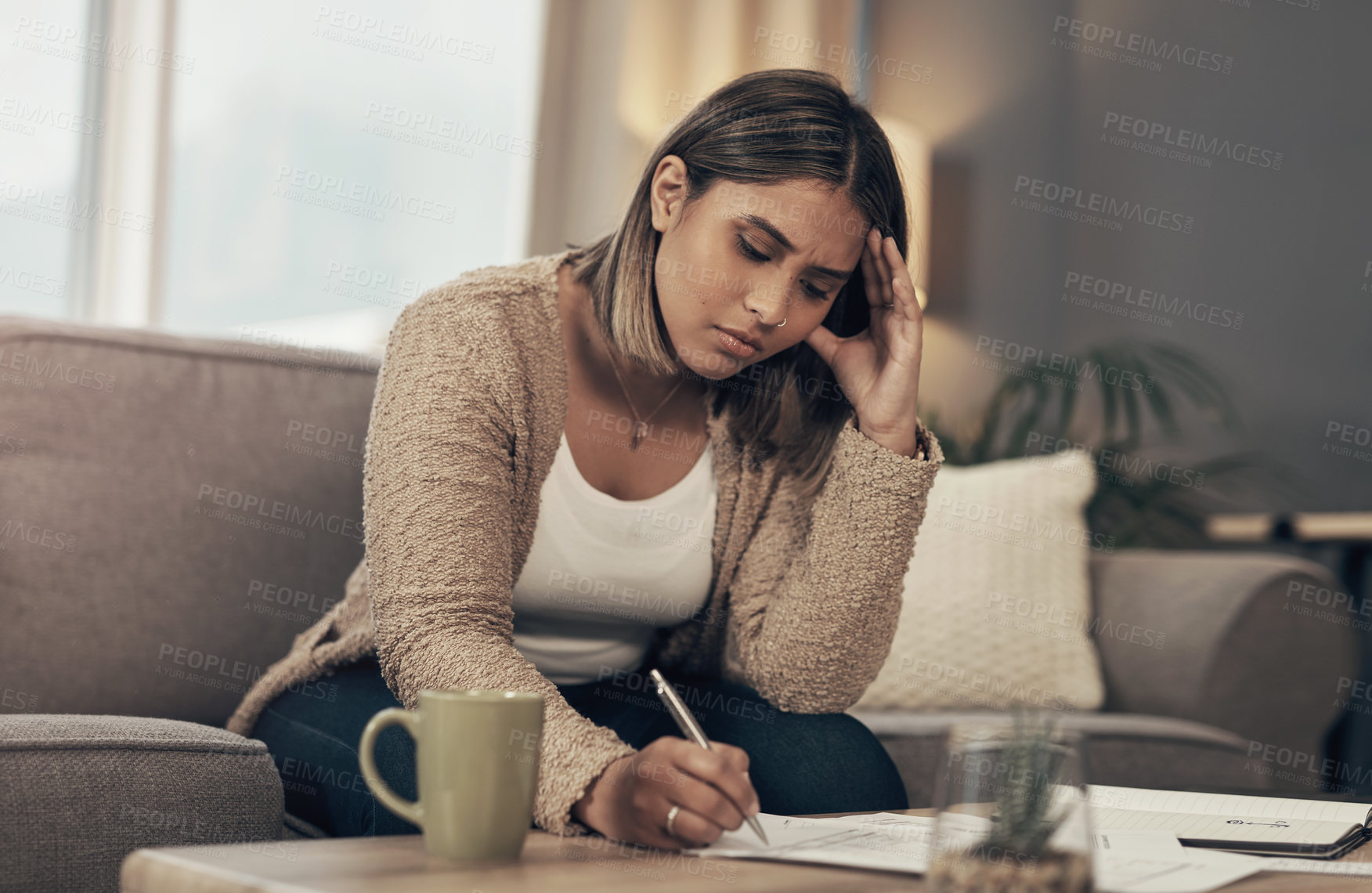 Buy stock photo Shot of a young woman looking stressed while going over paperwork at home