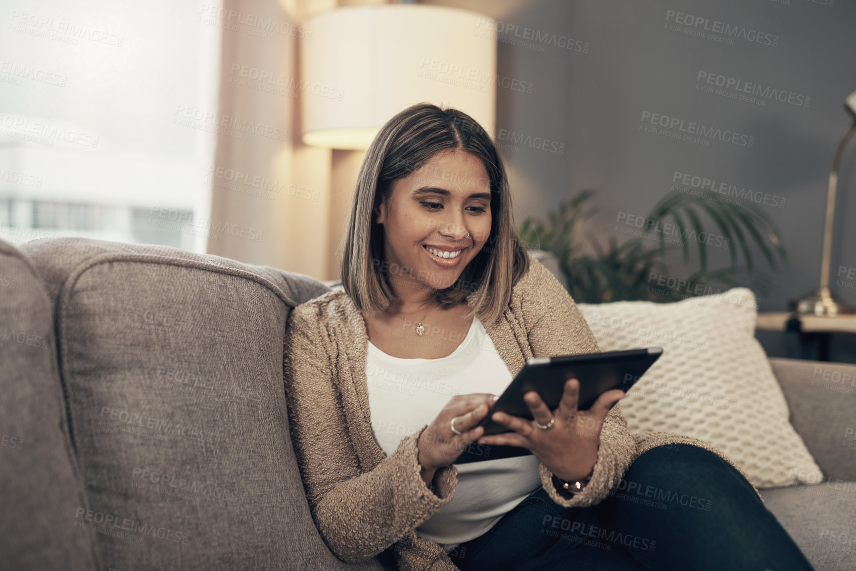 Buy stock photo Shot of a young woman using a digital tablet on the sofa at home