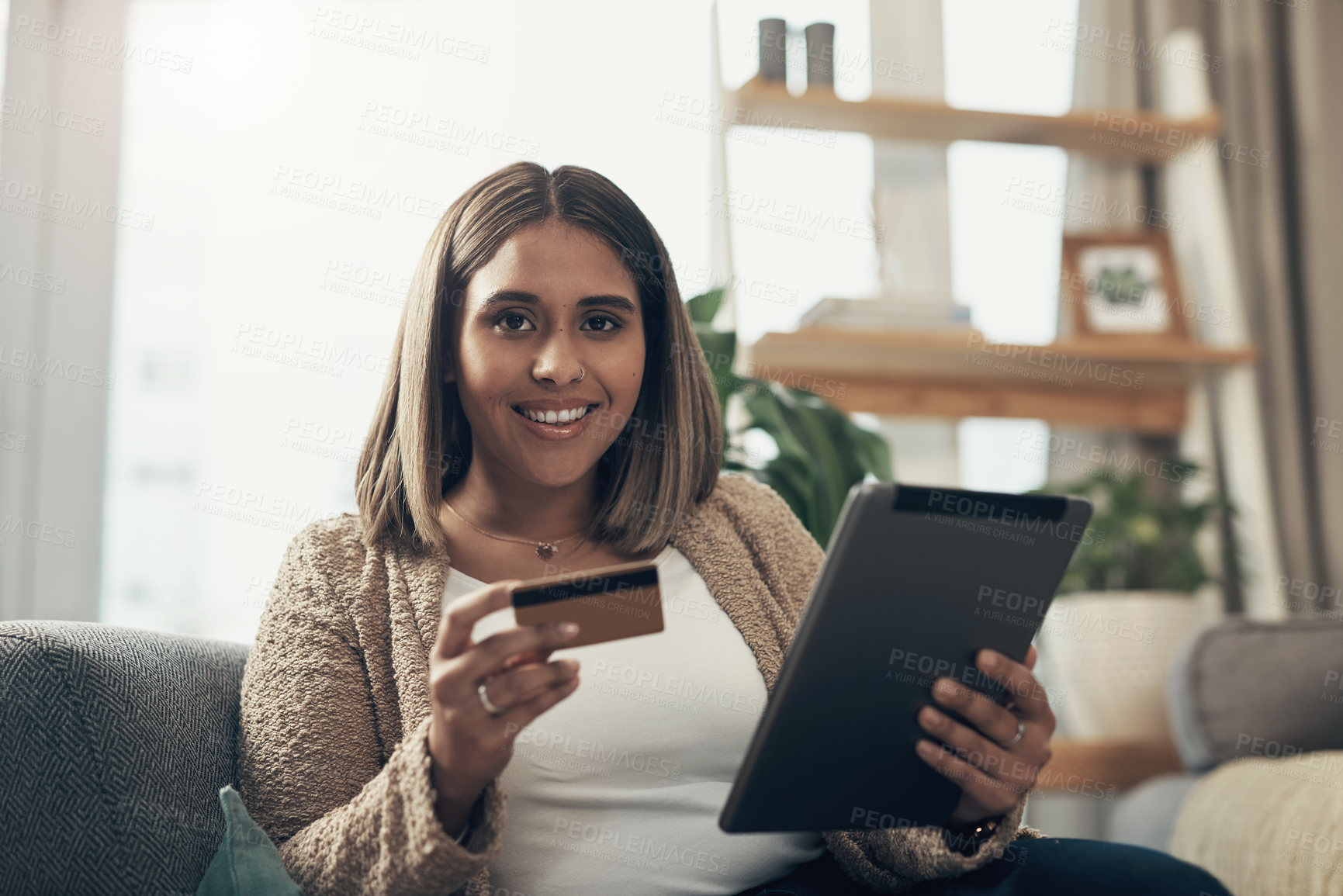 Buy stock photo Shot of a young woman using a digital tablet and credit card on the sofa at home