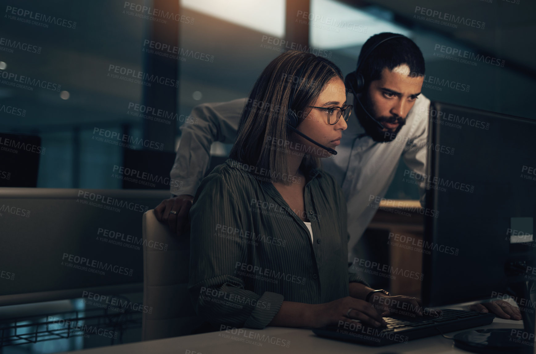 Buy stock photo Shot of two call centre agents working together in an office at night