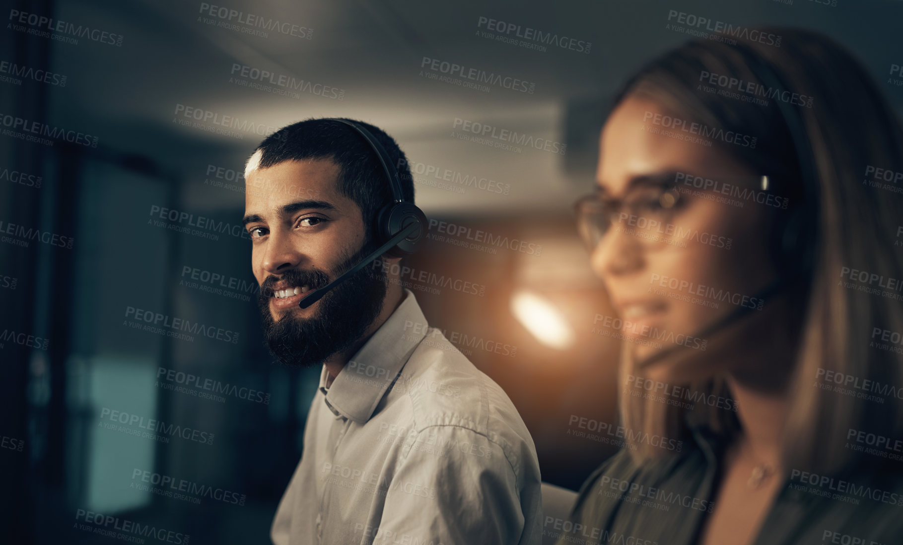 Buy stock photo Portrait of a call centre agent working in an office alongside a colleague at night