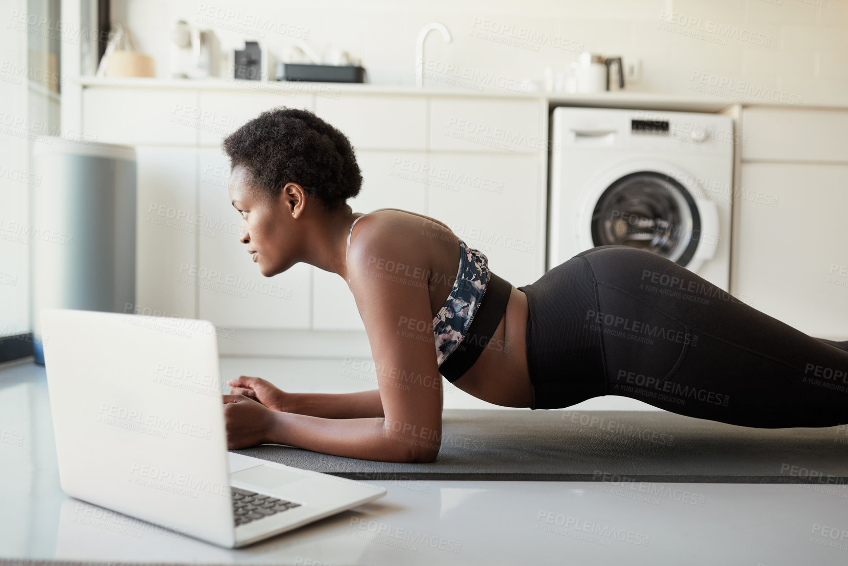 Buy stock photo Shot of a young woman using a laptop while exercising at home