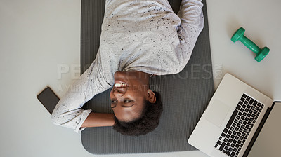 Buy stock photo High angle shot of a young woman lying on an exercise mat with a laptop, cellphone and dumbbell around her