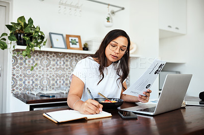 Buy stock photo Shot of a young woman going through paperwork and writing notes while working from home