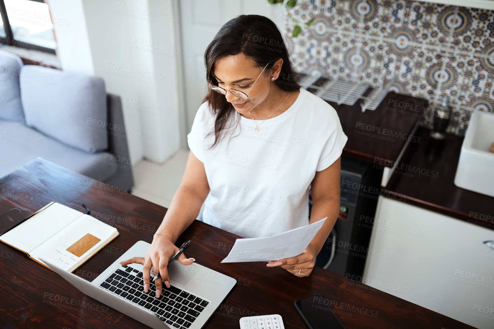 Buy stock photo Shot of a young woman going through paperwork while working from home