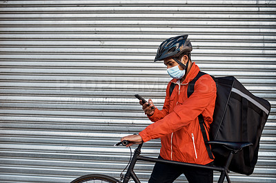 Buy stock photo Shot of a masked man using his cellphone while out on his bicycle for a delivery
