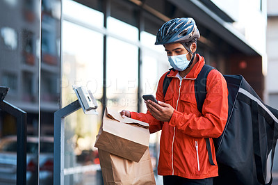 Buy stock photo Shot of a masked man using his cellphone while doing a food delivery