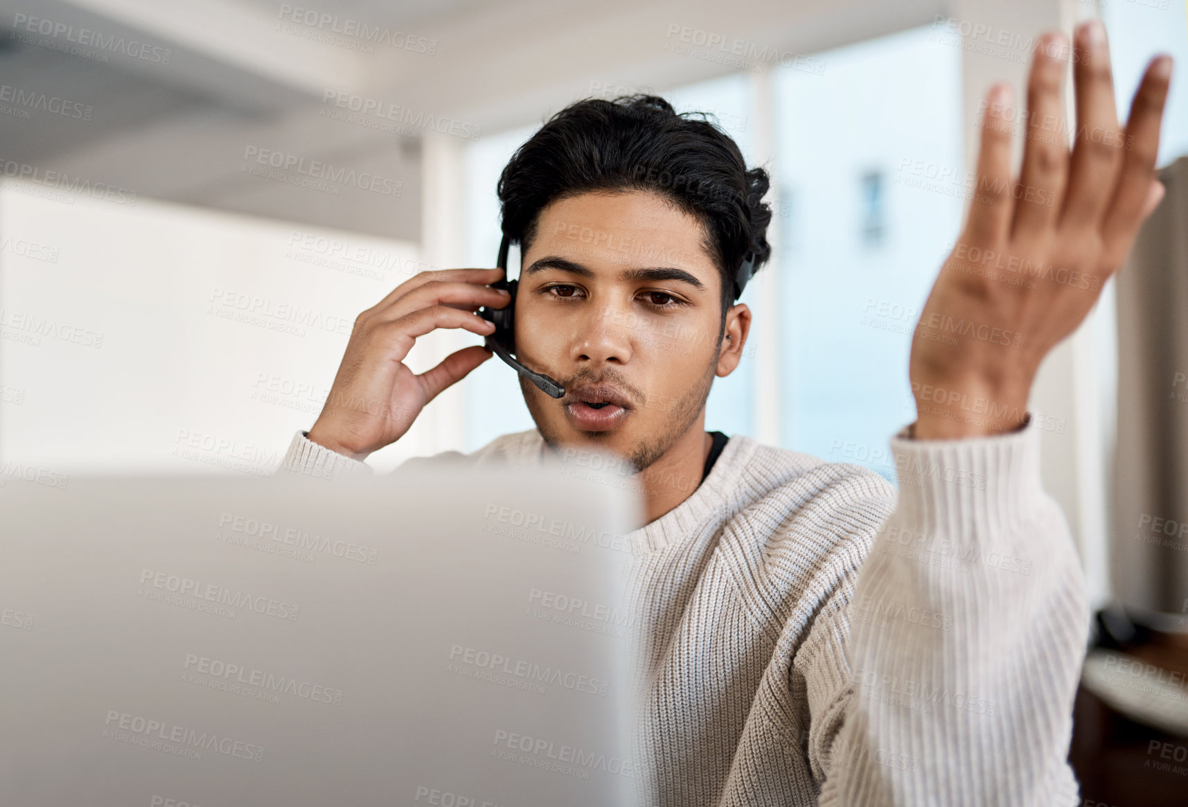 Buy stock photo Shot of a young man wearing a headset while working on a laptop at home