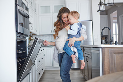 Buy stock photo Shot of a pregnant woman baking while spending spending time with her toddler son at home