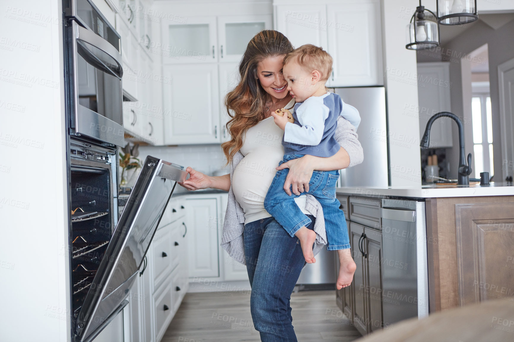Buy stock photo Shot of a pregnant woman baking while spending spending time with her toddler son at home