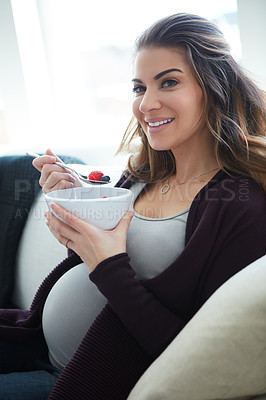 Buy stock photo Cropped portrait of an attractive young pregnant woman eating breakfast while sitting on the sofa at home