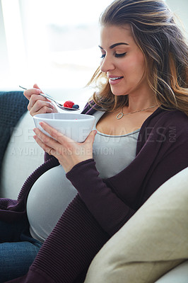 Buy stock photo Cropped shot of an attractive young pregnant woman eating breakfast while sitting on the sofa at home