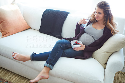 Buy stock photo Full length shot of an attractive young pregnant woman eating breakfast while sitting on the sofa at home