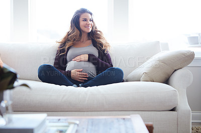 Buy stock photo Full length shot of an attractive young pregnant woman sitting on the sofa at home
