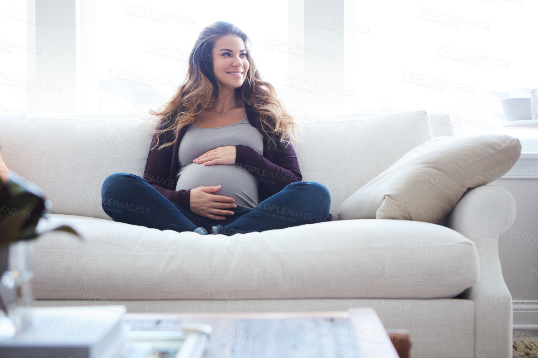 Buy stock photo Full length shot of an attractive young pregnant woman sitting on the sofa at home