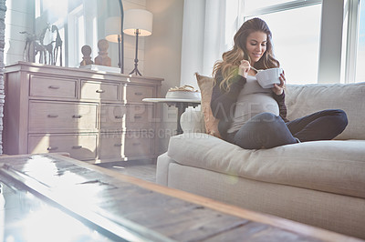 Buy stock photo Full length shot of an attractive young pregnant woman eating breakfast while sitting on the sofa at home