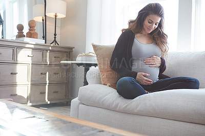 Buy stock photo Full length shot of an attractive young pregnant woman sitting on the sofa at home